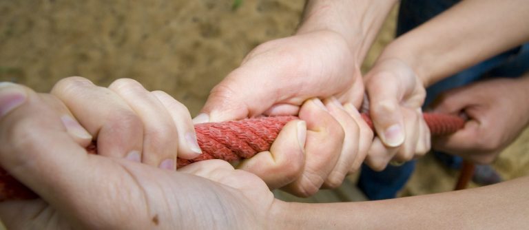 Vier Hände, die an einem roten Seil ziehen